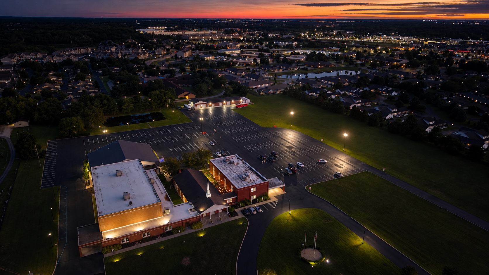 Twilight aerial photograph of an illuminated church campus beneath a vivid Columbus, Ohio sunset